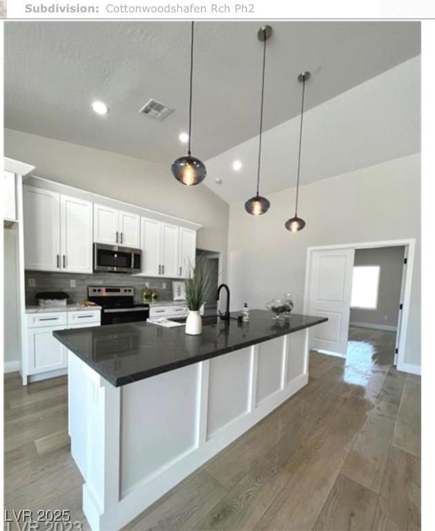 3791 Soplo Rd, Pahrump, NV 89048 - kitchen featuring appliances with stainless steel finishes, lofted ceiling, white cabinetry, dark countertops, and a spacious island