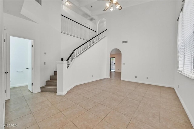 3935 Tirana Way, Las Vegas, NV 89103 - unfurnished living room featuring ceiling fan, arched walkways, a high ceiling, light tile patterned flooring, and stairway