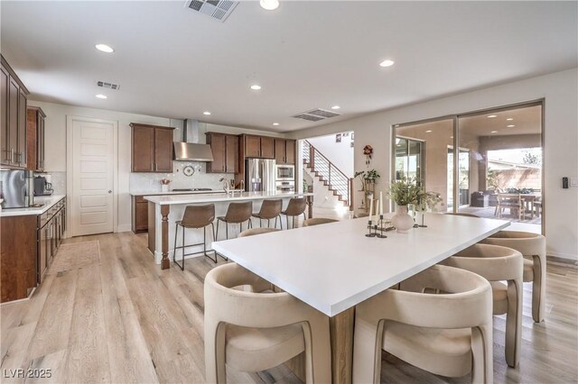 9655 Skye Star Ave, Las Vegas, NV 89166 - kitchen with wall chimney exhaust hood, appliances with stainless steel finishes, a large island with sink, light wood-style flooring, and recessed lighting