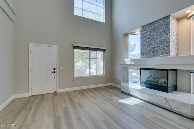 10908 Royal Highlands St, Las Vegas, NV 89141 - unfurnished living room featuring a towering ceiling, wood finished floors, plenty of natural light, a glass covered fireplace, and baseboards