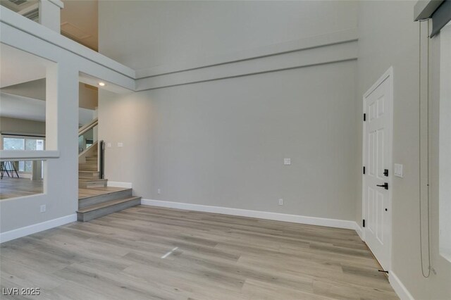 10908 Royal Highlands St, Las Vegas, NV 89141 - unfurnished living room featuring light wood-type flooring, stairway, baseboards, and a towering ceiling
