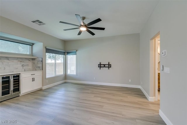 10908 Royal Highlands St, Las Vegas, NV 89141 - unfurnished living room with wine cooler, a ceiling fan, light wood-type flooring, baseboards, and a bar