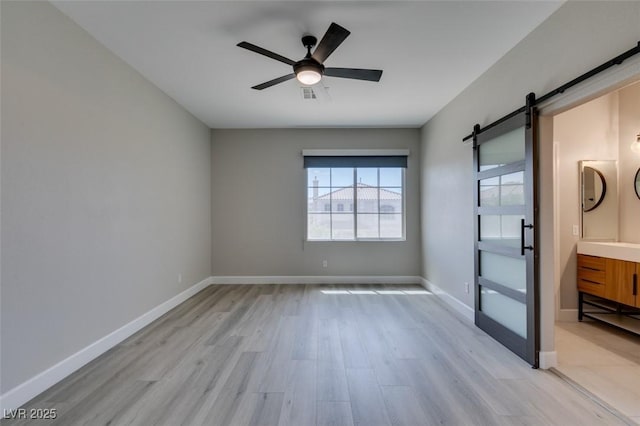 10908 Royal Highlands St, Las Vegas, NV 89141 - unfurnished room with a barn door, light wood-style flooring, a ceiling fan, and baseboards