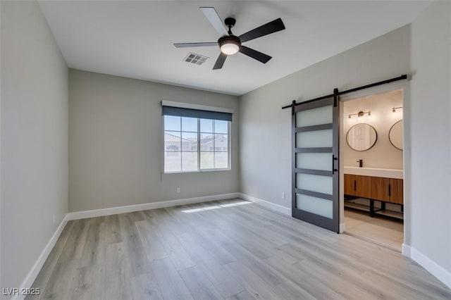 10908 Royal Highlands St, Las Vegas, NV 89141 - unfurnished bedroom featuring a barn door, light wood-style floors, and baseboards