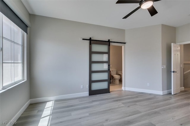 10908 Royal Highlands St, Las Vegas, NV 89141 - unfurnished bedroom featuring a barn door, light wood finished floors, baseboards, and ensuite bath