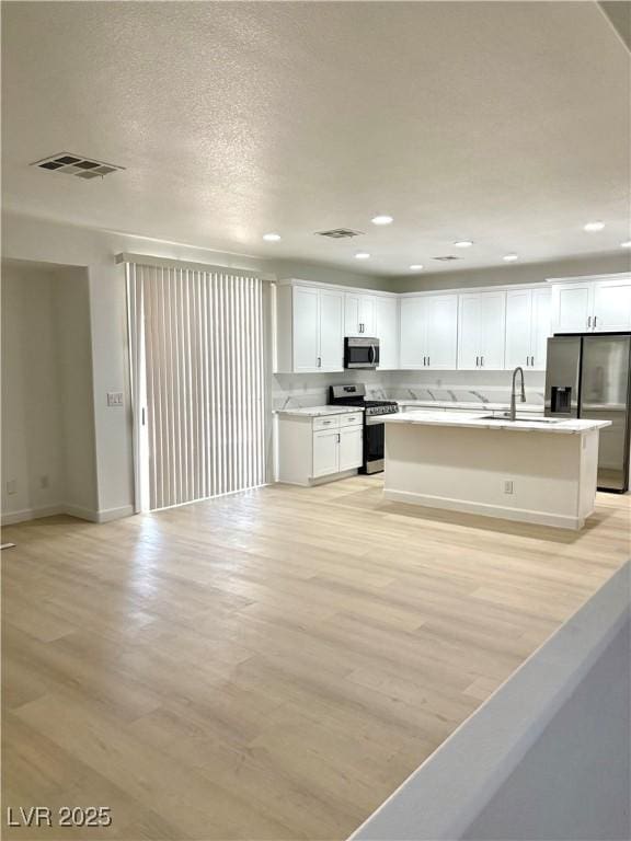 7615 Paso Robles Ave, Las Vegas, NV 89113 - kitchen featuring appliances with stainless steel finishes, light wood finished floors, open floor plan, white cabinets, and light countertops