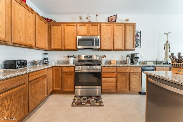 2413 Mourning Warbler Ave, North Las Vegas, NV 89084 - kitchen featuring appliances with stainless steel finishes, brown cabinetry, light stone countertops, and light tile patterned floors