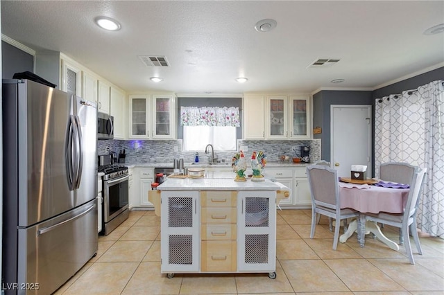 3404 Brayton Mist Dr, North Las Vegas, NV 89081 - kitchen featuring stainless steel appliances, crown molding, tasteful backsplash, glass insert cabinets, and recessed lighting