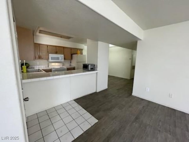 2725 S Nellis Blvd Unit 1158, Las Vegas, NV 89121 - kitchen featuring white appliances, tile countertops, dark wood-style flooring, brown cabinets, and a peninsula