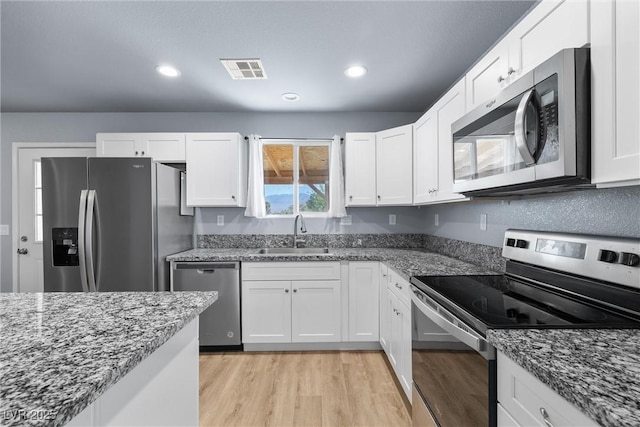 100 Eton St, Pahrump, NV 89048 - kitchen with stainless steel appliances, light wood-style floors, white cabinetry, dark stone counters, and recessed lighting