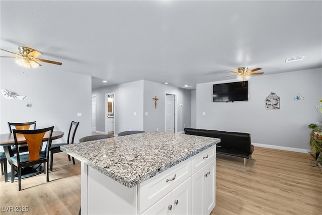 100 Eton St, Pahrump, NV 89048 - kitchen featuring a ceiling fan, a center island, light wood-type flooring, white cabinets, and light stone counters