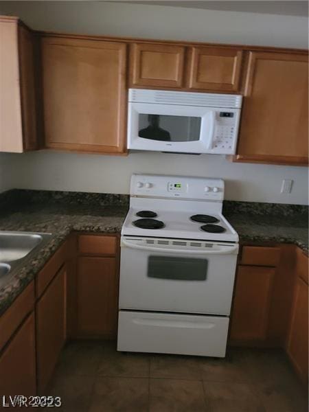 7730 Secret Shore Dr Unit 207, Las Vegas, NV 89128 - kitchen featuring white appliances, tile patterned floors, brown cabinets, dark stone countertops, and a sink