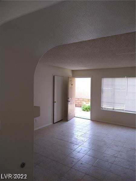 1608 N Torrey Pines Dr Unit 103, Las Vegas, NV 89108 - empty room featuring arched walkways, baseboards, a textured ceiling, and tile patterned floors