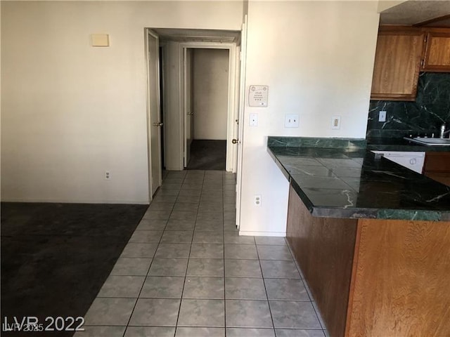 1105 Sulphur Springs Ln Unit 102, Las Vegas, NV 89128 - kitchen with tile patterned flooring, dark countertops, backsplash, and brown cabinetry