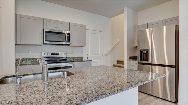 4229 Venus Falls Ave, North Las Vegas, NV 89084 - kitchen featuring appliances with stainless steel finishes, gray cabinets, a sink, light stone counters, and light wood-style flooring
