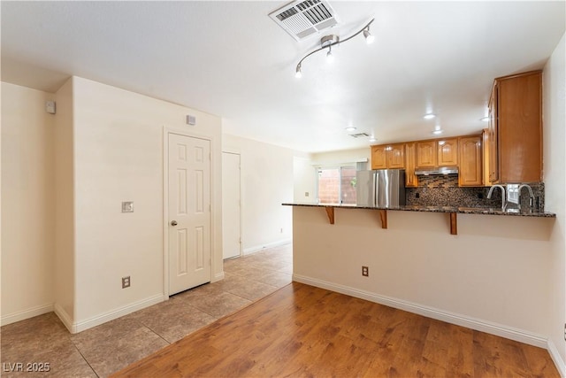 7923 Homer Ct, Las Vegas, NV 89139 - kitchen with freestanding refrigerator, under cabinet range hood, a peninsula, a breakfast bar area, and dark stone countertops