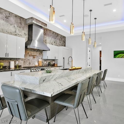 5400 Mello Ave, Las Vegas, NV 89131 - kitchen with wall chimney range hood, a kitchen breakfast bar, backsplash, a raised ceiling, and white cabinets