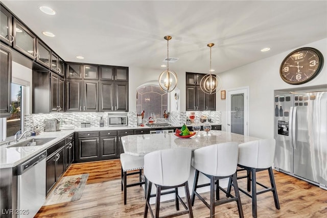 5889 Thistle Meadow Ave, Las Vegas, NV 89139 - kitchen with appliances with stainless steel finishes, light wood-style flooring, decorative backsplash, a breakfast bar area, and light stone counters