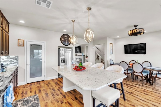 5889 Thistle Meadow Ave, Las Vegas, NV 89139 - kitchen with stainless steel fridge with ice dispenser, a breakfast bar, recessed lighting, a center island, and light stone countertops