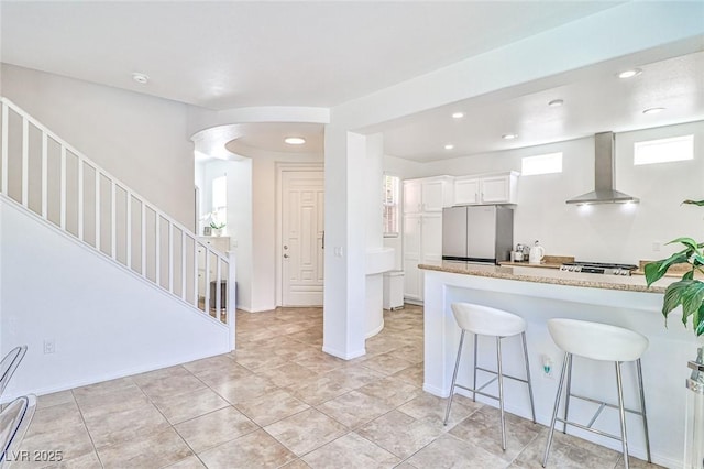 10667 Olympic Pine Dr, Las Vegas, NV 89135 - kitchen featuring wall chimney exhaust hood, freestanding refrigerator, a kitchen breakfast bar, white cabinetry, and recessed lighting