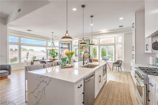 3028 Treesdale Dr, Las Vegas, NV 89134 - kitchen featuring appliances with stainless steel finishes, a sink, light wood-style floors, a kitchen island with sink, and white cabinetry