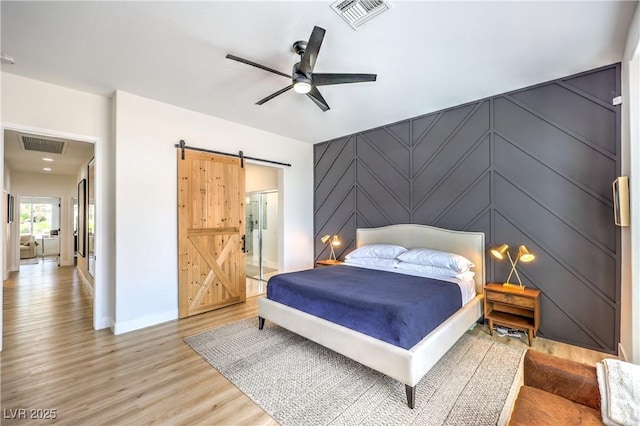 3028 Treesdale Dr, Las Vegas, NV 89134 - bedroom with a barn door, light wood-type flooring, baseboards, a decorative wall, and ceiling fan