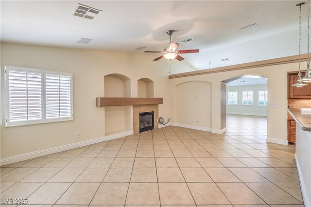 1044 Spanish Needle St, Henderson, NV 89002 - unfurnished living room with ceiling fan, a tiled fireplace, light tile patterned floors, arched walkways, and baseboards