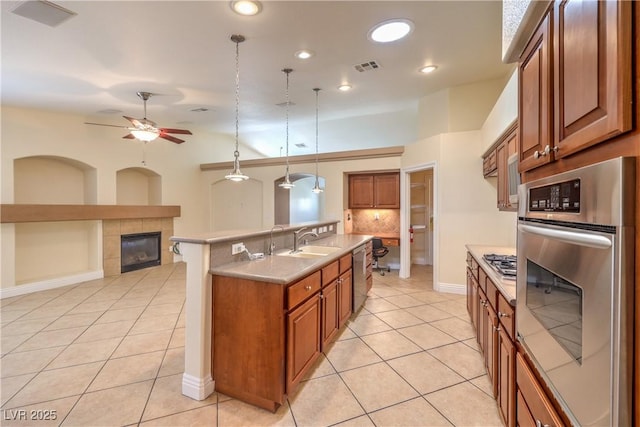 1044 Spanish Needle St, Henderson, NV 89002 - kitchen featuring appliances with stainless steel finishes, light tile patterned floors, a tile fireplace, brown cabinets, and recessed lighting