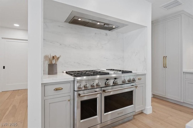 204 Canyon Dr, Las Vegas, NV 89107 - kitchen featuring range with two ovens, range hood, light wood finished floors, decorative backsplash, and light countertops