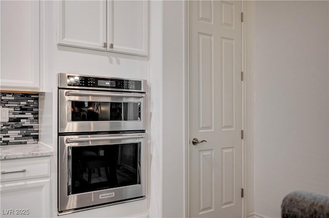 505 Sterling Falls Ave, Henderson, NV 89011 - kitchen with stainless steel double oven, white cabinetry, tasteful backsplash, and light stone countertops
