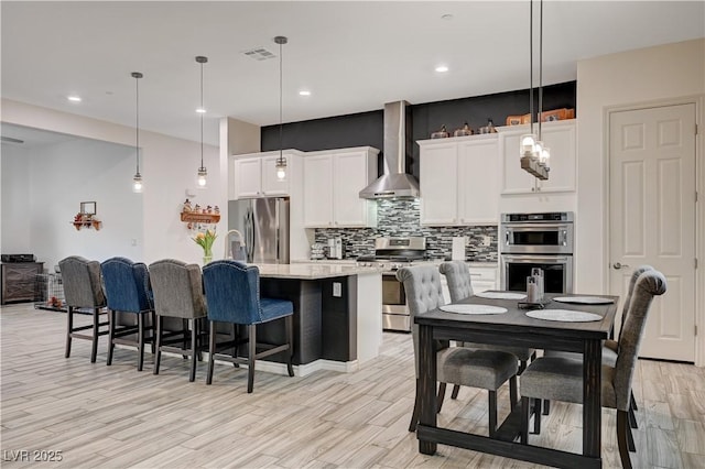 505 Sterling Falls Ave, Henderson, NV 89011 - kitchen with appliances with stainless steel finishes, wall chimney exhaust hood, an island with sink, decorative backsplash, and white cabinets