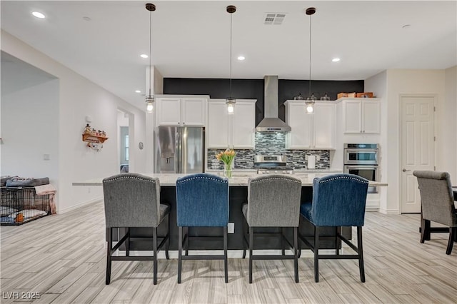 505 Sterling Falls Ave, Henderson, NV 89011 - kitchen featuring appliances with stainless steel finishes, wall chimney range hood, white cabinetry, backsplash, and light wood-type flooring