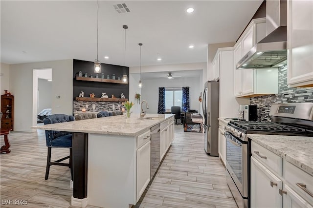 505 Sterling Falls Ave, Henderson, NV 89011 - kitchen with appliances with stainless steel finishes, wall chimney range hood, a kitchen breakfast bar, decorative backsplash, and light wood-type flooring