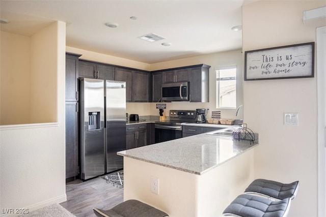 2629 Mocha Pearl Ct, North Las Vegas, NV 89086 - kitchen featuring stainless steel appliances, a sink, a peninsula, light stone countertops, and dark brown cabinetry