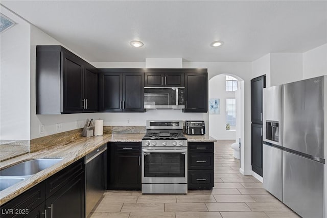 9428 Sierra Summit Ave, Las Vegas, NV 89134 - kitchen with stainless steel appliances, dark cabinetry, light stone counters, arched walkways, and recessed lighting