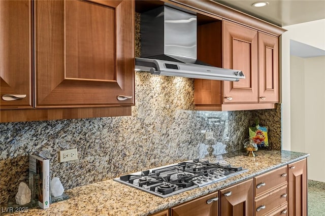 2777 Paradise Rd Unit 2302, Las Vegas, NV 89109 - kitchen with stainless steel gas stovetop, wall chimney exhaust hood, backsplash, brown cabinetry, and light stone counters