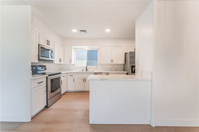 4301 Fortune Ave, Las Vegas, NV 89107 - kitchen with appliances with stainless steel finishes, a sink, white cabinets, a peninsula, and light wood-style floors