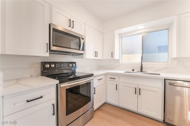 4301 Fortune Ave, Las Vegas, NV 89107 - kitchen with stainless steel appliances, a sink, white cabinets, light stone counters, and light wood-style flooring