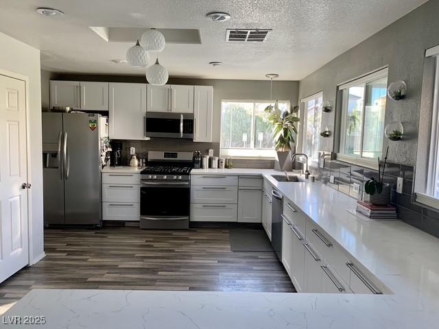 9485 Supernova Ct, Las Vegas, NV 89123 - kitchen featuring appliances with stainless steel finishes, decorative backsplash, plenty of natural light, dark wood-style flooring, and a textured ceiling