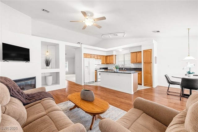 5704 Owl Butte Ct, Las Vegas, NV 89149 - living room with light wood-type flooring, a ceiling fan, a glass covered fireplace, vaulted ceiling, and baseboards