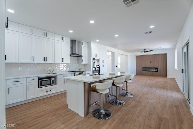 1136 Casady Hollow Ave, Henderson, NV 89012 - kitchen featuring wall chimney exhaust hood, stainless steel appliances, light wood-type flooring, a kitchen breakfast bar, and a ceiling fan