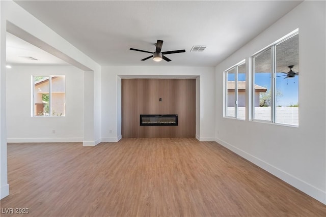 1136 Casady Hollow Ave, Henderson, NV 89012 - unfurnished living room featuring ceiling fan, light wood-style flooring, a glass covered fireplace, and baseboards