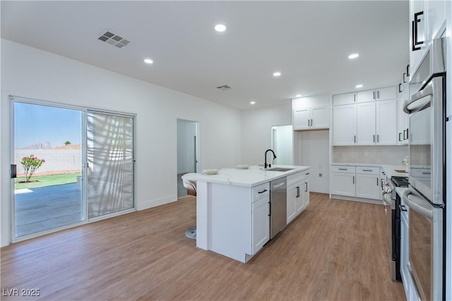 1136 Casady Hollow Ave, Henderson, NV 89012 - kitchen featuring a sink, appliances with stainless steel finishes, light wood-style flooring, a kitchen island with sink, and white cabinets