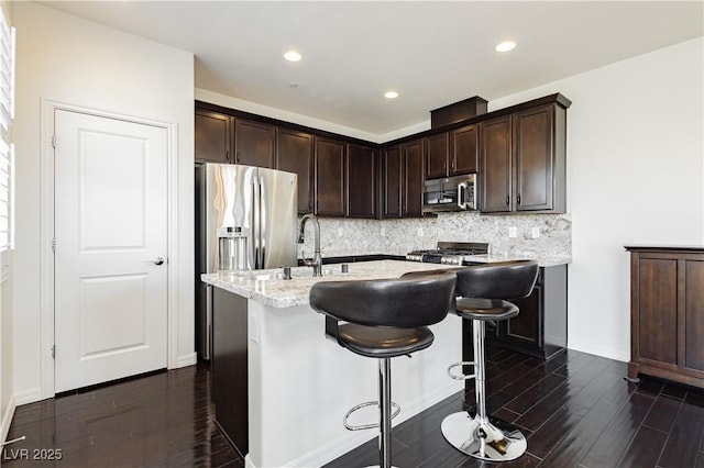 1185 Via Dimartini, Henderson, NV 89052 - kitchen with appliances with stainless steel finishes, dark wood-style flooring, backsplash, dark brown cabinetry, and a kitchen island with sink