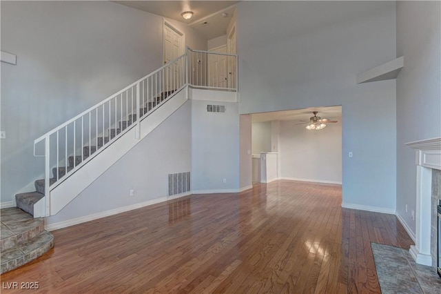 7968 Lisa Dawn Ave, Las Vegas, NV 89147 - unfurnished living room featuring a tiled fireplace, stairs, wood-type flooring, a ceiling fan, and a towering ceiling