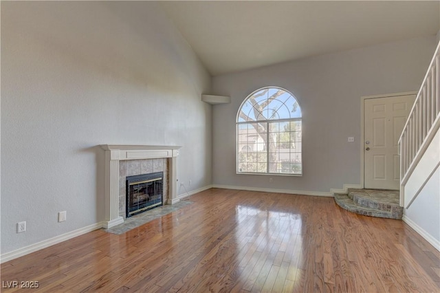 7968 Lisa Dawn Ave, Las Vegas, NV 89147 - unfurnished living room featuring wood finished floors, stairway, a tile fireplace, baseboards, and high vaulted ceiling