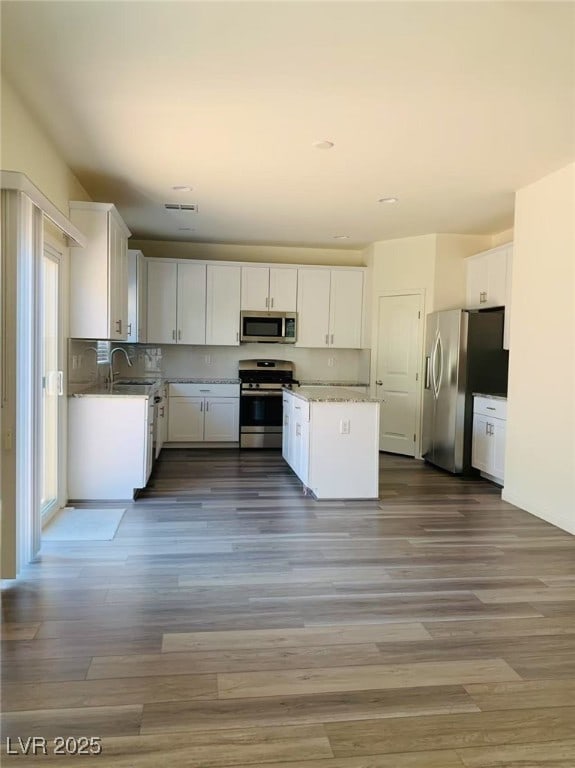 8793 Candelabra Ct, Las Vegas, NV 89148 - kitchen featuring appliances with stainless steel finishes, a sink, white cabinets, wood finished floors, and a kitchen island