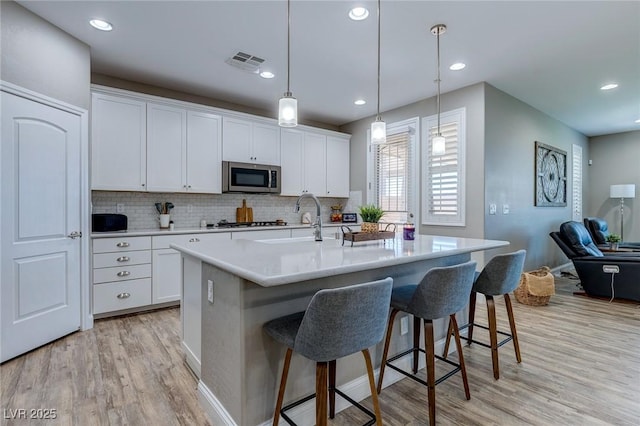 379 Mano Destra Ln, Henderson, NV 89011 - kitchen featuring appliances with stainless steel finishes, light wood-type flooring, a kitchen bar, tasteful backsplash, and white cabinets