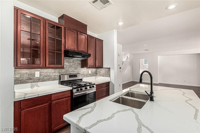 9173 Weeping Hollow Ave, Las Vegas, NV 89178 - kitchen featuring under cabinet range hood, a sink, stainless steel gas range oven, tasteful backsplash, and glass insert cabinets