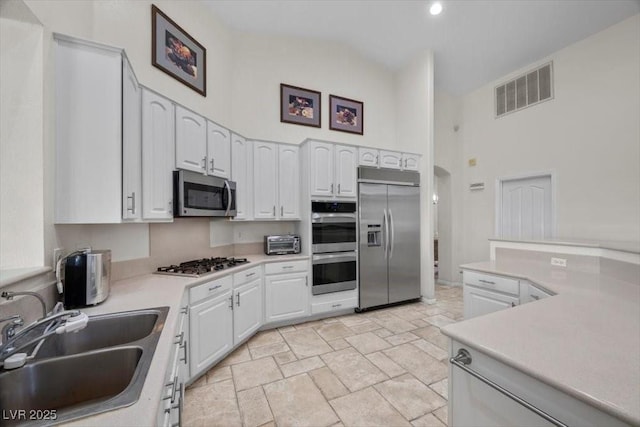 835 Market Crest Dr, Las Vegas, NV 89110 - kitchen with stainless steel appliances, a sink, high vaulted ceiling, white cabinets, and light stone finish floors